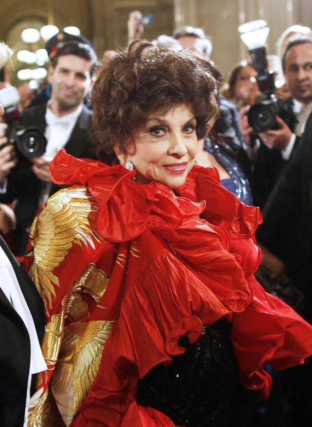 Gina Lollobrigida in einem roten Kleid mit goldenen Stickereien, umgeben von Fotografen.