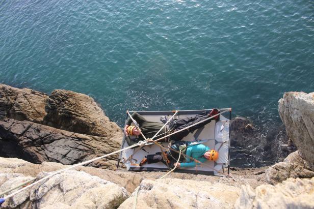 Zwei Personen entspannen sich in Hängematten, die an einer Klippe über dem Meer befestigt sind.