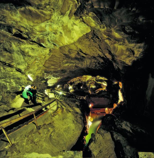 Zwei Personen steigen in einer Höhle eine Holztreppe hinab.