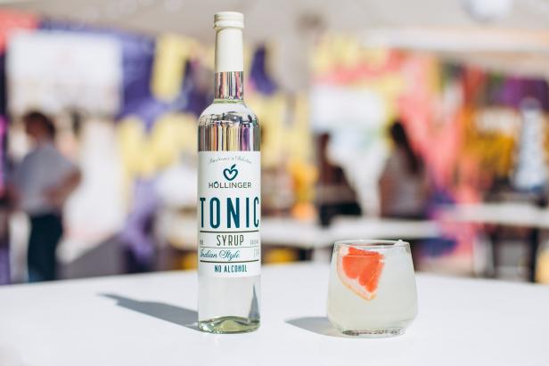 Eine Flasche Hollinger Tonic Sirup neben einem Glas mit einem Getränk und Grapefruitspalte.