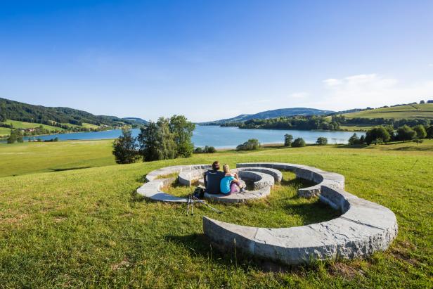 Ein Paar sitzt auf einer spiralförmigen Steinbank mit Blick auf einen See.