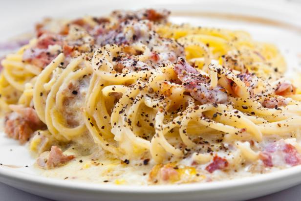 Ein Teller Spaghetti Carbonara, garniert mit Speck und schwarzem Pfeffer.