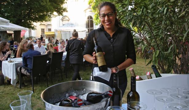 Eine Kellnerin präsentiert eine Flasche Wein auf einer Gartenparty.