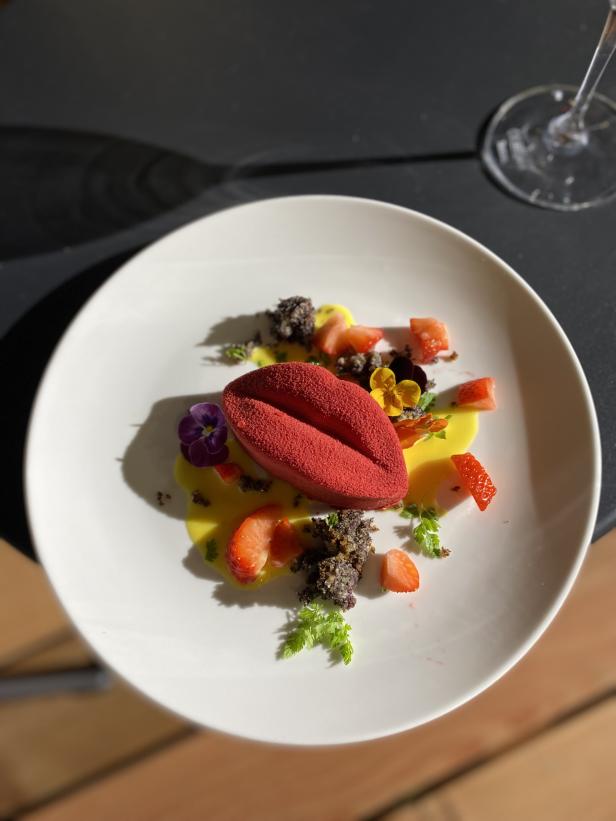 Ein Teller mit einem roten Dessert in Lippenform, Erdbeeren und essbaren Blüten garniert.