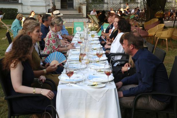 Gäste sitzen an einer langen, gedeckten Tafel im Freien.