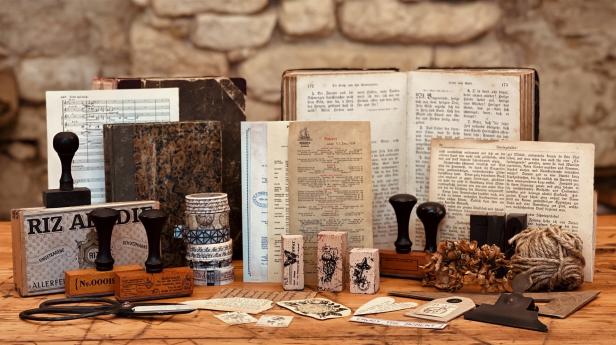 Eine Ansammlung von Vintage-Objekten wie Stempel, Briefe, Notenblätter und Bücher auf einem Holztisch.