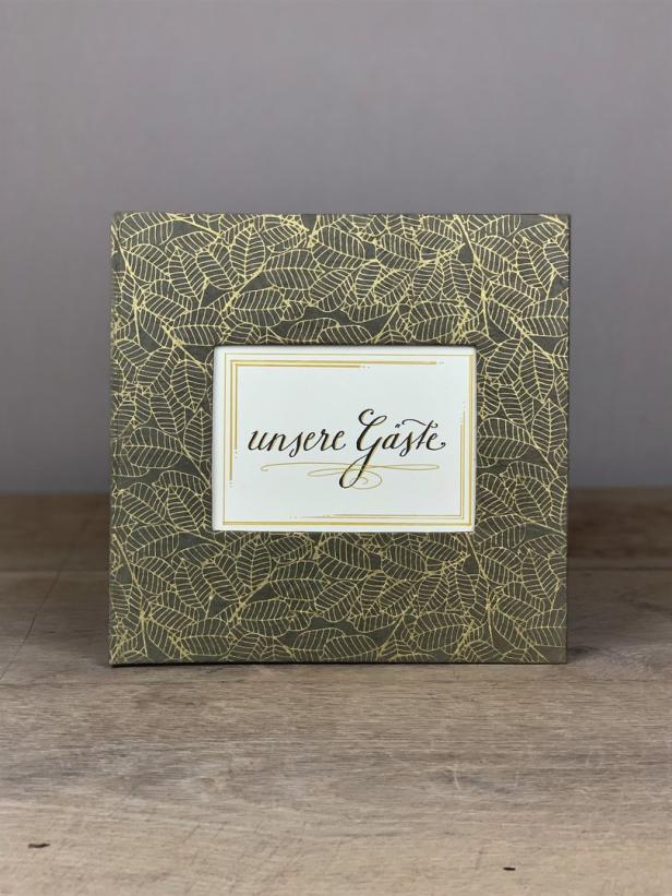 Ein Gästebuch mit goldenem Blättermuster und der Aufschrift „unsere Gäste“.