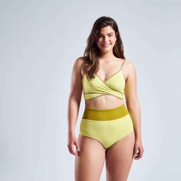 Eine Frau mit braunen Haaren trägt einen gelben Bikini vor einem hellgrauen Hintergrund.