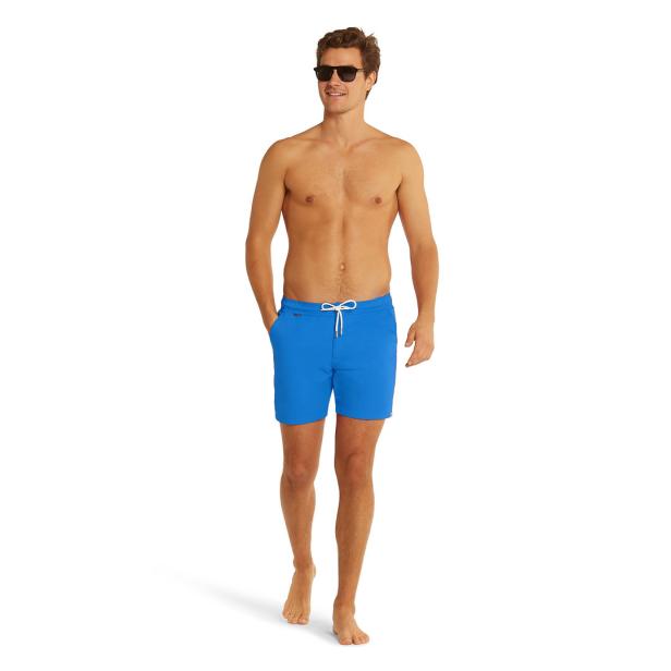 Ein Mann mit Sonnenbrille und blauer Badehose steht barfuß da.