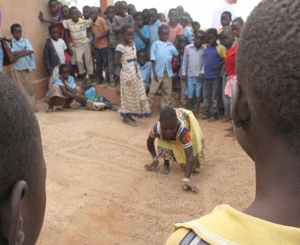 Eine Frau spielt ein Spiel im Sand, während eine Gruppe Kinder zusieht.