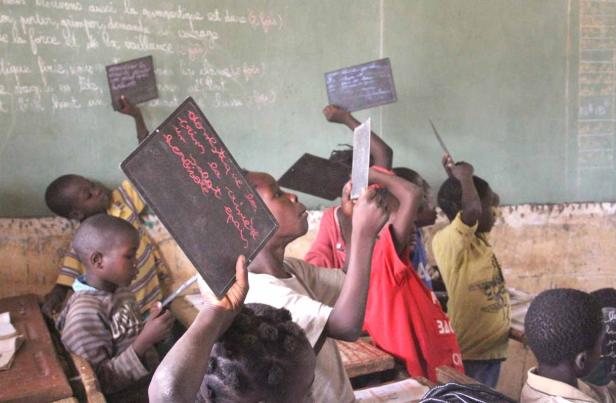 Kinder in einem Klassenzimmer halten Schiefertafeln hoch.