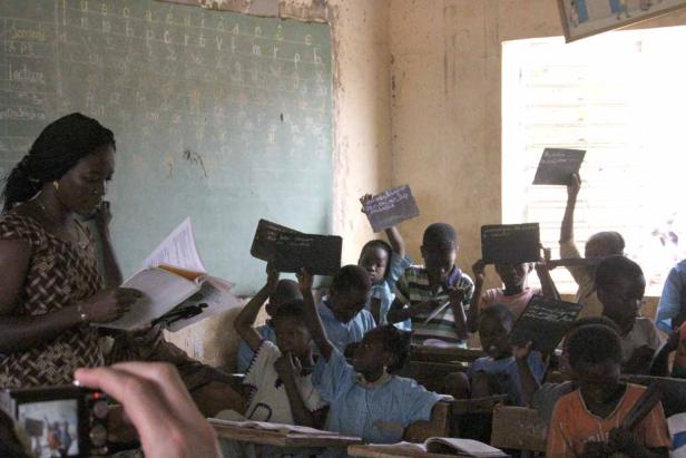Eine Lehrerin liest vor einer Klasse, die Schiefertafeln hochhält.