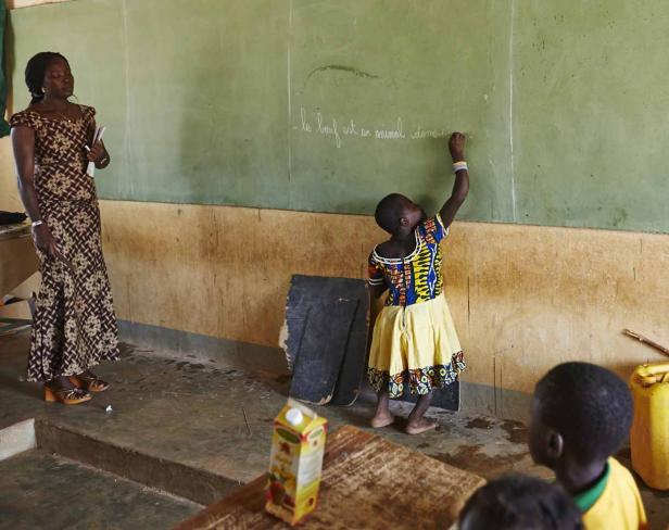 Ein Mädchen schreibt an einer Tafel, während eine Lehrerin zusieht.