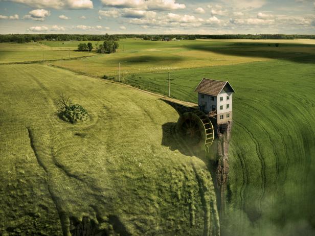 Ein Haus mit einem Wasserrad steht am Rande einer Klippe inmitten einer grünen Landschaft.