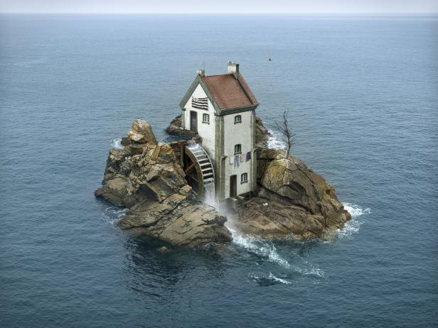 Ein Haus mit einem Wasserrad steht auf einer felsigen Insel im Meer.