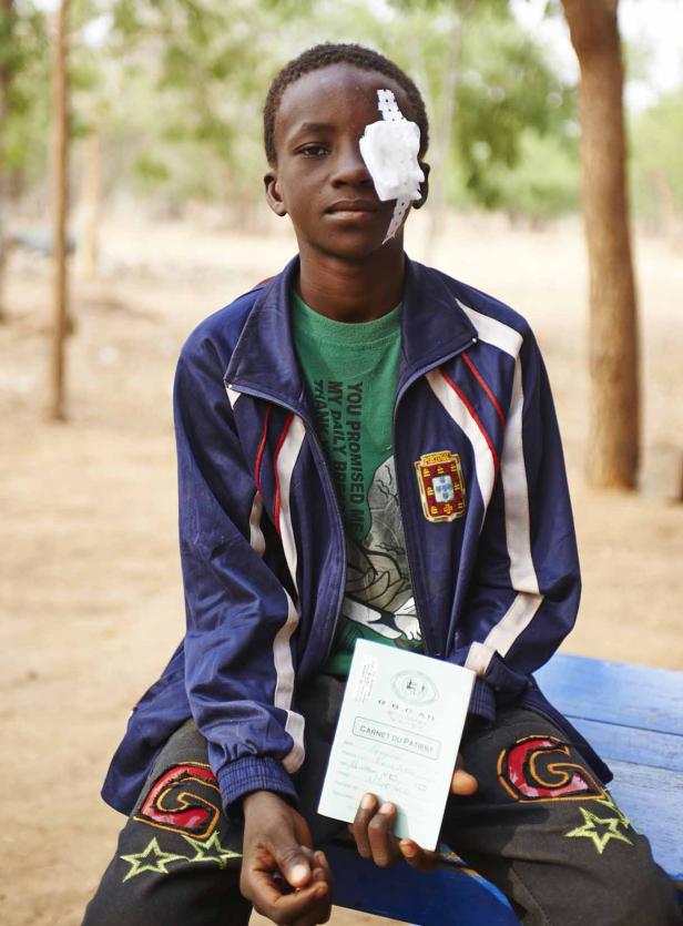 Ein junger Mann mit einem Verband über dem Auge hält eine Patientenakte in der Hand.