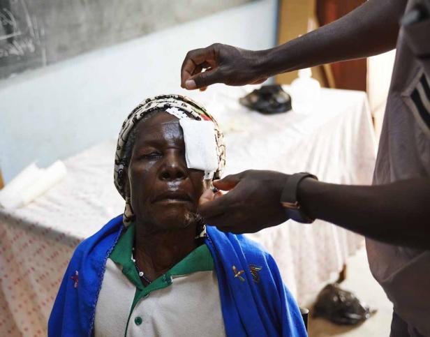 Einer älteren Frau wird ein Augenverband angelegt.