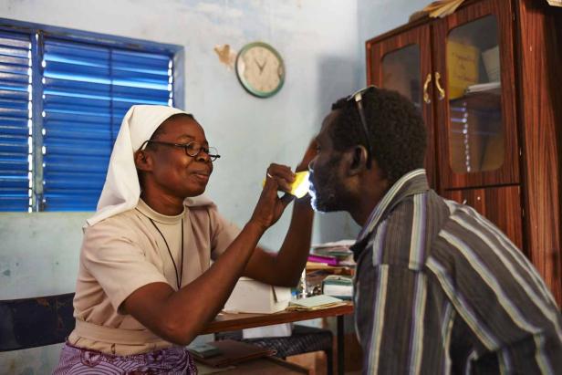 Eine Ordensschwester untersucht mit einer kleinen Lampe den Mund eines Mannes.