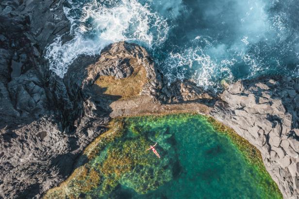 Eine Frau schwimmt in einem natürlichen Pool umgeben von Felsen und dem Meer.