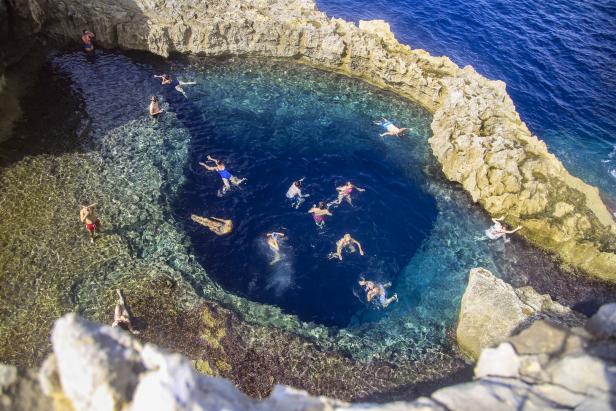 Eine Gruppe von Menschen schwimmt in einem natürlichen Felsenpool mit klarem, blauem Wasser.