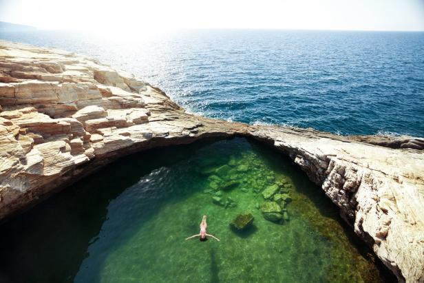 Eine Frau schwimmt in einem natürlichen Felsenpool am Meer.