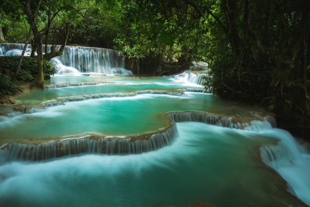 Ein mehrstufiger Wasserfall mit türkisfarbenem Wasser fließt durch einen üppigen grünen Wald.