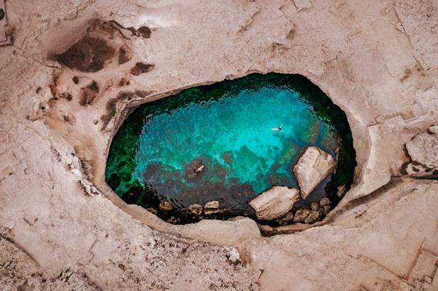 Eine Person schwimmt in einem natürlichen, von Felsen umgebenen Pool mit türkisfarbenem Wasser.