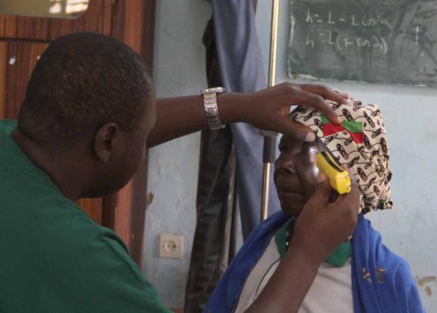 Ein Arzt untersucht das Auge einer älteren Frau mit einer kleinen Lampe.