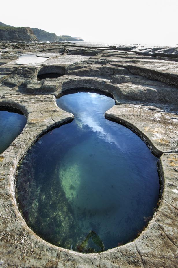Ein von Felsen umgebener Gezeitentümpel mit klarem, blauem Wasser.