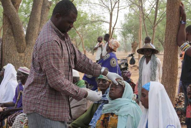Ein Mann untersucht mit Handschuhen die Stirn einer älteren Frau im Freien.