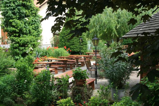 Ein Biergarten mit Holztischen und üppiger Vegetation.