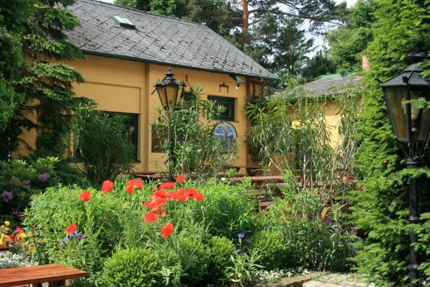 Ein gelbes Gebäude mit einem Garten voller Mohnblumen und anderen Pflanzen.