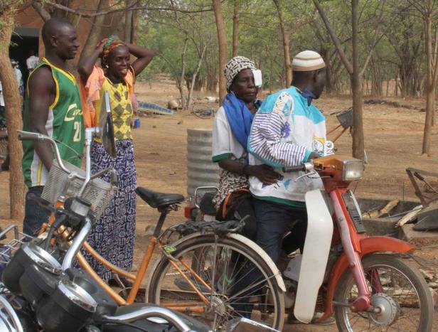 Eine Gruppe von Menschen steht neben Fahrrädern und einem Moped im Freien.
