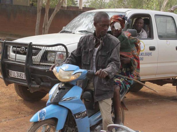 Ein Mann fährt mit einem Moped, während eine Frau mit einer Augenverletzung und ein Baby mitfahren.