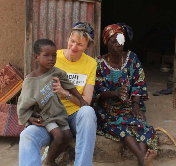 Eine Frau mit einem Jungen auf dem Schoß sitzt neben einer älteren Frau mit einem Augenverband.