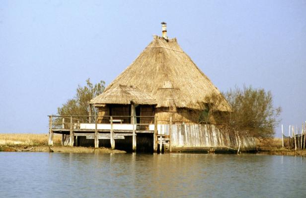 Ein Haus mit Strohdach steht auf Stelzen im Wasser.