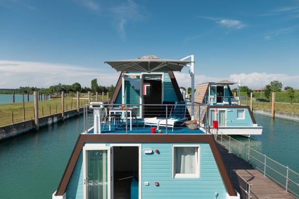 Mehrere hellblaue Hausboote liegen auf einem Kanal unter blauem Himmel.