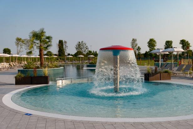 Ein Schwimmbad mit einem Wasserpilz und Liegestühlen unter Sonnenschirmen.