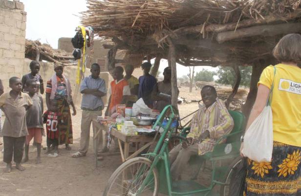 Eine Gruppe von Menschen steht vor einem kleinen Laden unter einem Strohdach.