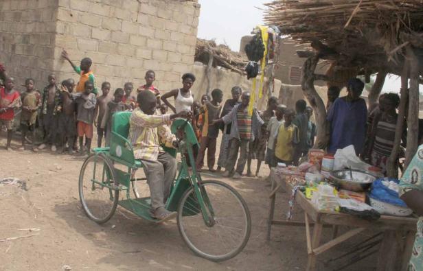 Ein Junge fährt ein grünes Dreirad, während eine Gruppe von Menschen zusieht.
