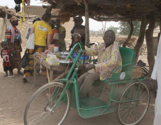 Ein Mann sitzt in einem grünen Dreirad vor einem Verkaufsstand im Freien.