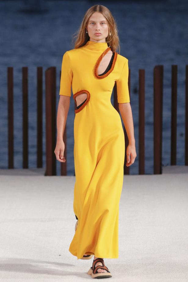 Eine Frau in einem gelben Kleid mit Cut-Outs auf einem Laufsteg.