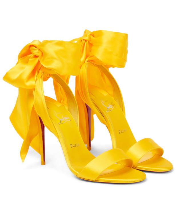 Ein Paar gelbe Christian Louboutin Sandalen mit Schleifen an den Knöcheln.