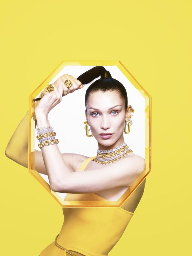 Bella Hadid präsentiert gelben Schmuck vor einem gelben Hintergrund.