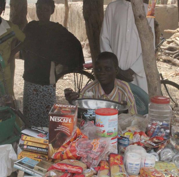 Ein junger Mann sitzt an einem Stand mit Lebensmitteln und anderen Waren.