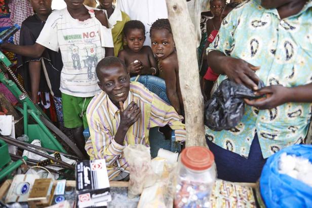 Ein Mann sitzt hinter einem Verkaufsstand, umgeben von Kindern und Waren.