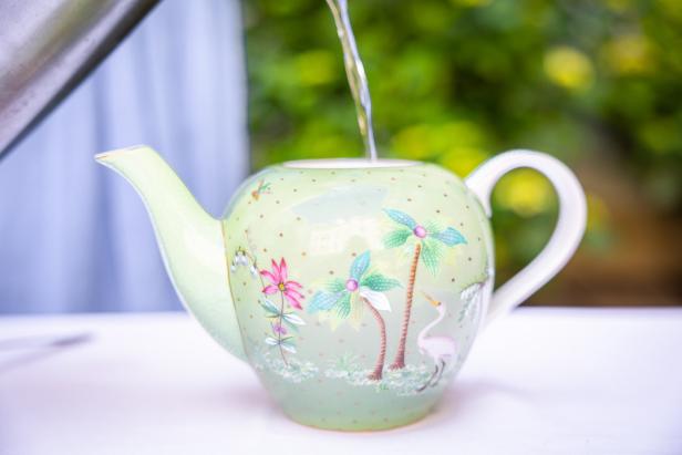 Wasser wird in eine hellgrüne Teekanne mit Palmen- und Blumenmuster gegossen.