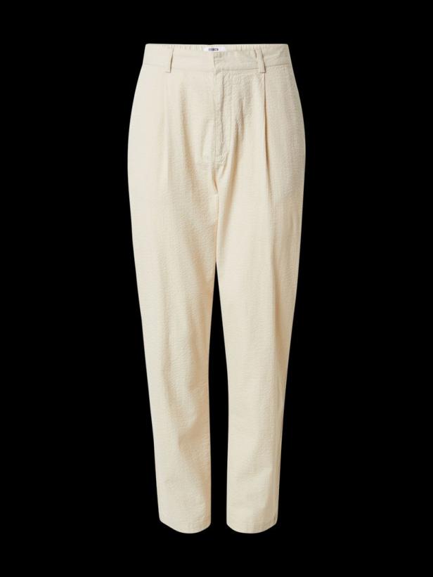 Eine hellbeige Stoffhose mit Bundfalten vor schwarzem Hintergrund.