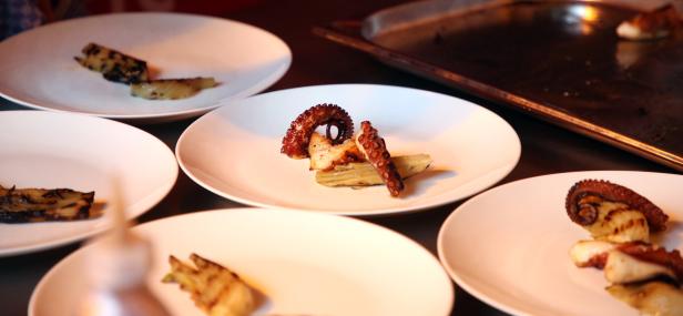 Mehrere Teller mit gegrilltem Tintenfisch und Artischocken werden angerichtet.