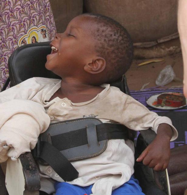 Ein lachender Junge sitzt in einem Rollstuhl.